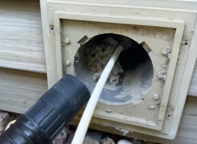 Dryer vent hood on a St. Augustine home exterior being cleared of lint with a cleaning rod